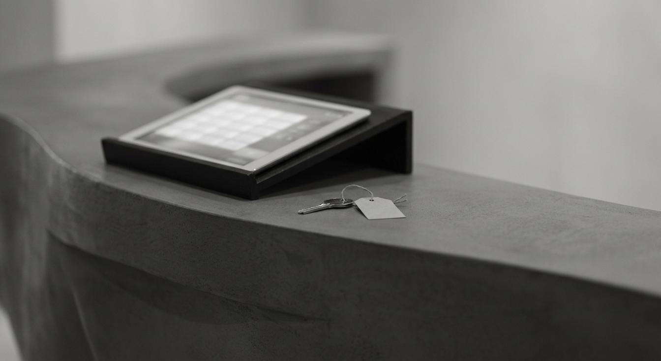 Abstract grayscale composition of a hotel reception desk with a tablet showing a rate calendar and a key with a price tag