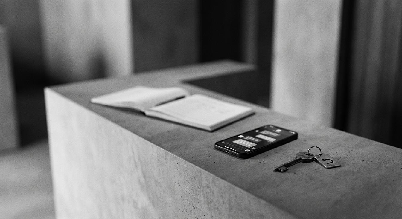 Composición abstracta en escala de grises de una recepción de hotel con un libro de huéspedes, un teléfono y una llave